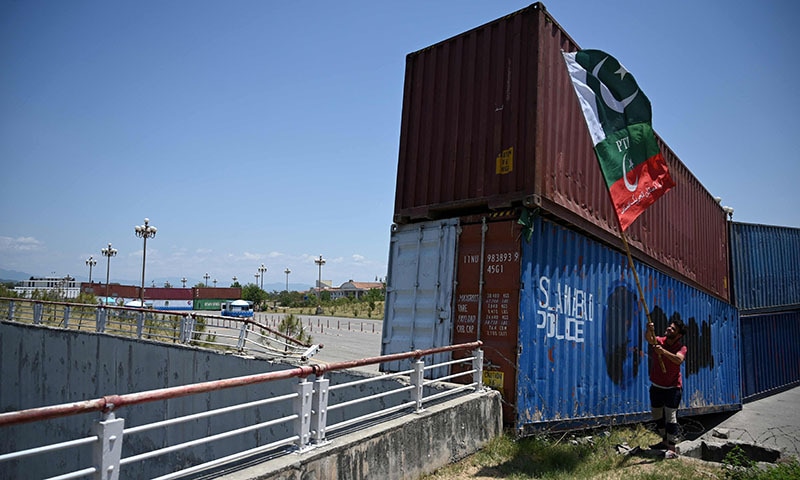 A PTI supporter waves flags beside containers stacked by the authorities to block the Red Zone ahead of the sit-in planned in Islamabad, on Tuesday. — AFP