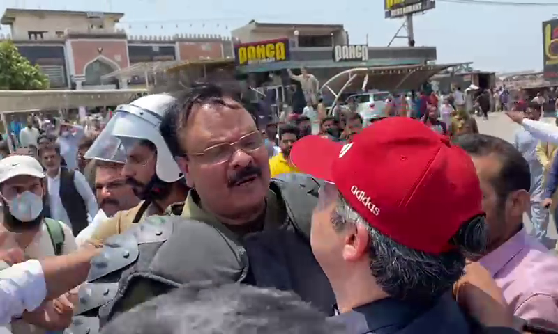 A police official in riot control gear attempting to detain Hammad Azhar (in red cap) on Wednesday. —DawnNewsTV