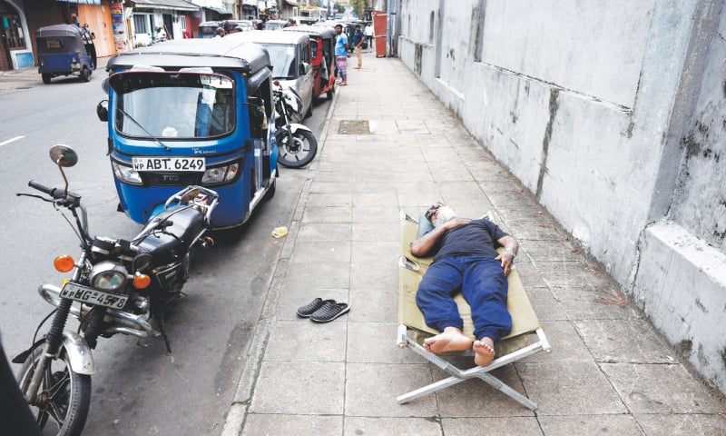 COLOMBO: A man sleeps on a folding bed on a sidewalk as he waits in line to buy petrol amid a fuel shortage on Friday.—Reuters