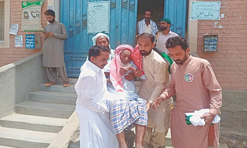 TWO men carry an old relative into a polling station in Larkana on Sunday.—Dawn