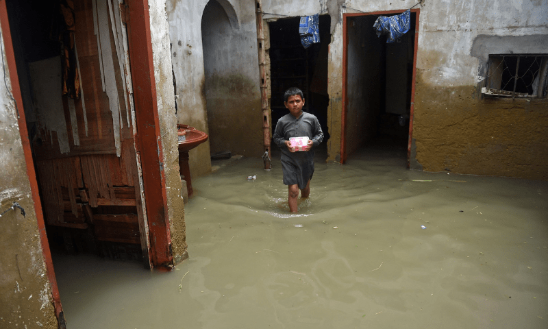 A boy wades through his flooded house after heavy monsoon rains in Karachi on Tuesday. — AFP