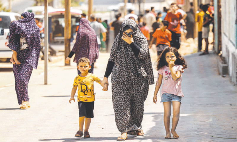 A Palestinian woman with two children covers her face as she walks away from a building hit by an Israeli air strike in Gaza City on Saturday.—AFP A Palestinian woman with two children covers her face as she walks away from a building hit by an Israeli air strike in Gaza City on Saturday.—AFP
