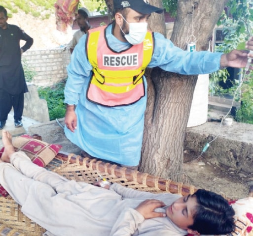 A Rescue 1122 worker carries schoolchildren across an inundated road after heavy rain in Peshawar on Wednesday. — Dawn