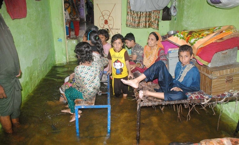 A family sits in rainwater after water enters their house in Latifabad, Hyderabad. — Photo by Umair Ali