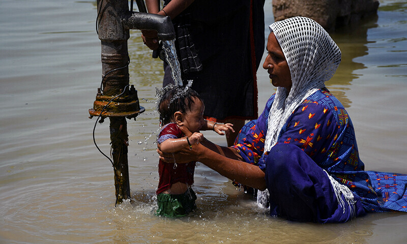 A woman gives a bath to her baby outside her flooded house in Khairpur Nathan Shah on Saturday.—Reuters