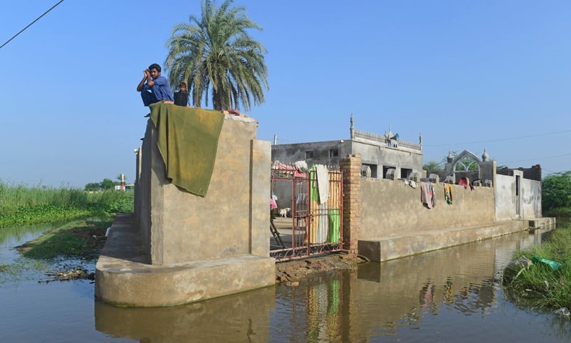 A flood-affected man along with a boy sits atop their house in flood-hit Sukkur on September 2, 2022. — AFP