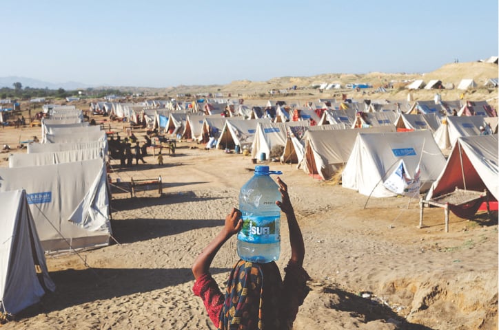 SEHWAN: A displaced girl carries a bottle of water filled with stagnant floodwater, as she makes her way to the displaced family’s tent in a camp, set up by the Al-Khidmat Foundation.—Reuters