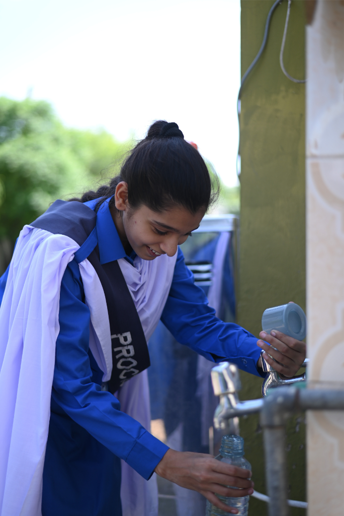       14-year-old Arzish Tahir smiles as she fills up her water bottle in school