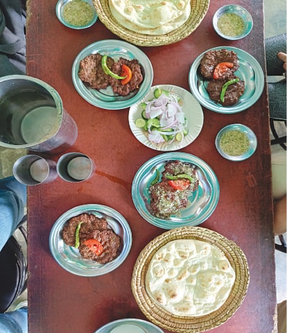 Chapli kebas served with sides of cucumber and onion salad and raita