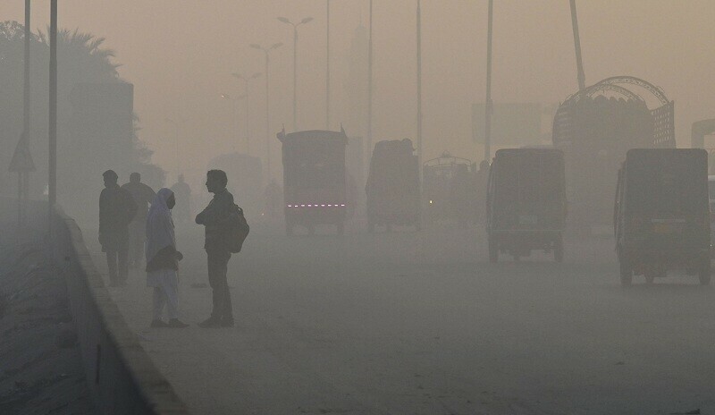 Students (L) wait for transport alongside a road amid heavy smog conditions in Lahore on Wednesday. — AFP