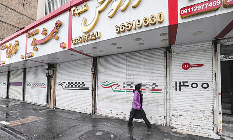 Tehran: A woman walks past closed shops along Satarkhan street in Iran’s capital on Monday.—AFP