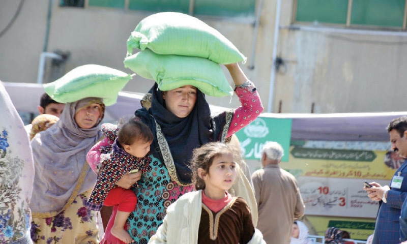 A woman holds her child as she carries flour bags on her head which she received from a distribution point in Rawalpindi on Saturday. — Online A woman holds her child as she carries flour bags on her head which she received from a distribution point in Rawalpindi on Saturday. — Online