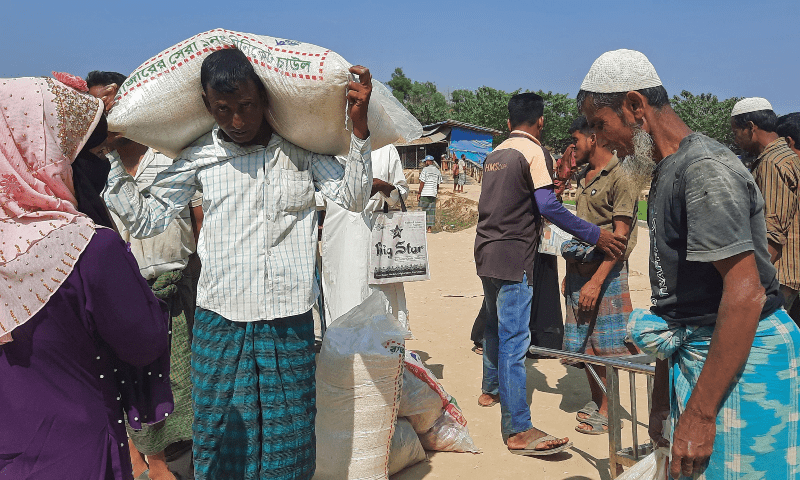 Rohingya refugees carry relief material after collecting from a distribution point in Kutupalong refugee camp in Ukhia on March 2, 2023. — AFP Rohingya refugees carry relief material after collecting from a distribution point in Kutupalong refugee camp in Ukhia on March 2, 2023. — AFP