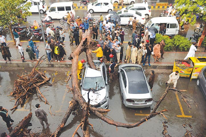 Lahore: Passers-by and rescue workers try to remove a tree that collapsed on top of a car parked along The Mall during a thunderstorm, which lashed the city on Tuesday.—Murtaza Ali / White Star