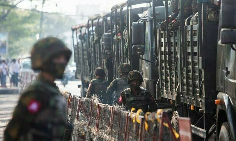 In this file photo, soldiers stand next to military vehicles as people gather to protest against the military coup in Yangon, Myanmar. &mdash; Reuters/File
