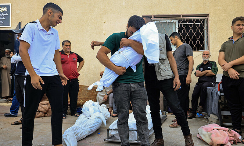 A man reacts as he carries the shrouded body of his child, in front of the morgue of the Al-Aqsa hospital in Deir Balah in the central Gaza Strip, following an Israeli strike on October 22. &mdash; AFP