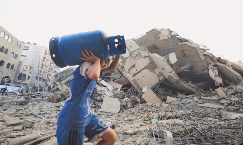 A boy carries a gas canister as he walks in front of a building that collapsed during an Israeli air strike in Gaza City, on Sunday.&mdash;AFP