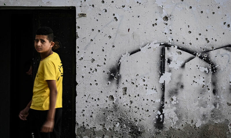 A boy walks past a shrapnel-riddled wall at the Jenin camp in the West Bank on November 4, 2023.&mdash;AFP