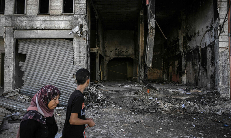 A Palestinian woman and a boy walk past a destroyed building at the Jenin camp in the West Bank on November 4, 2023.&mdash;AFP