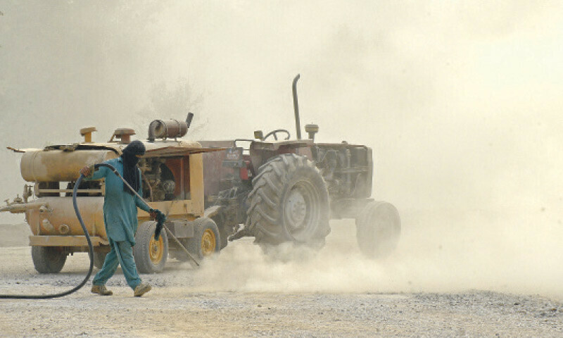 Dust rises as a labourer uses a blower to clean an under-construction road of the Rawal Dam interchange project. &mdash; File photo