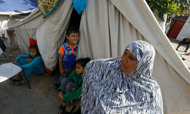 A woman stands with children at a school sheltering people who fled their houses due to Israeli strikes, in Rafah in the southern Gaza Strip, December 7, 2023. &mdash; Reuters