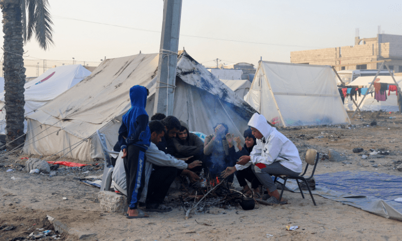 Displaced Palestinians, who fled their houses due to Israeli strikes, sit around a fire in a tent camp where they shelter in Rafah, in the southern Gaza Strip December 12. &mdash; Reuters