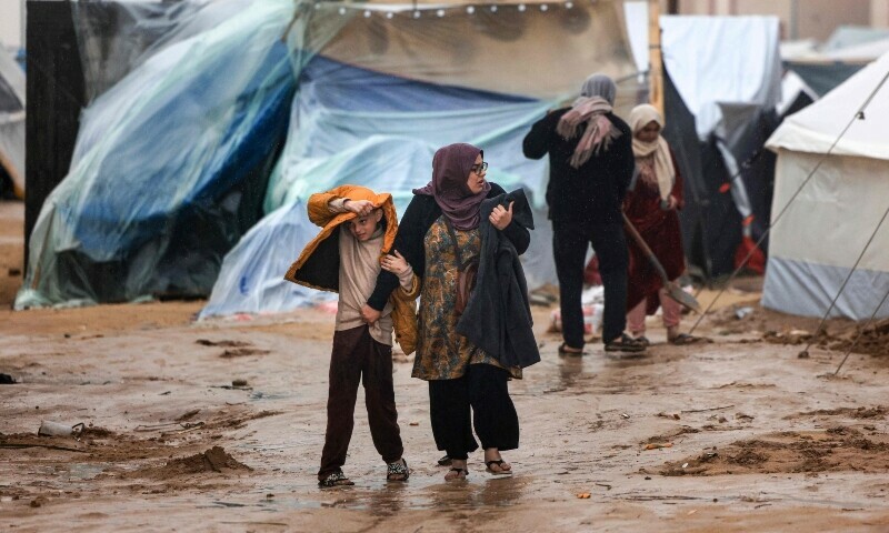 Palestinians walk under the rain at a camp for displaced people in Rafah, in the southern Gaza Strip where most civilians have taken refuge, on December 13, 2023.&mdash;AFP