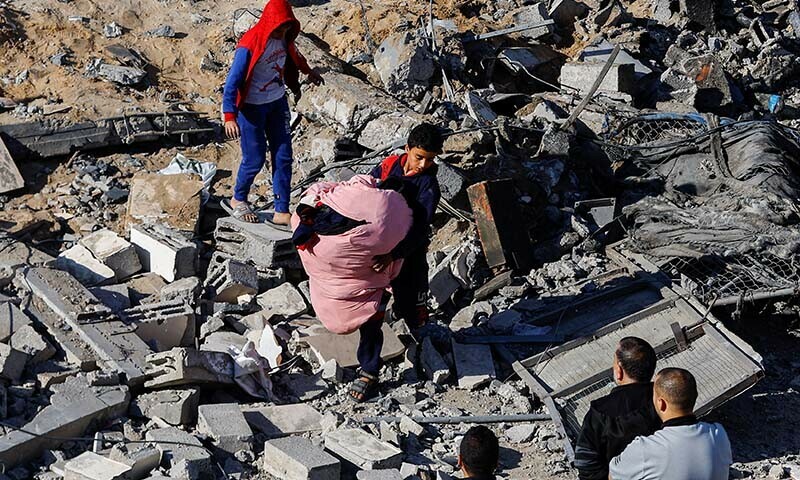 A Palestinian child carries items at the site of an Israeli strike on a house in Rafah, in the southern Gaza Strip on December 16, 2023 &mdash; Reuters