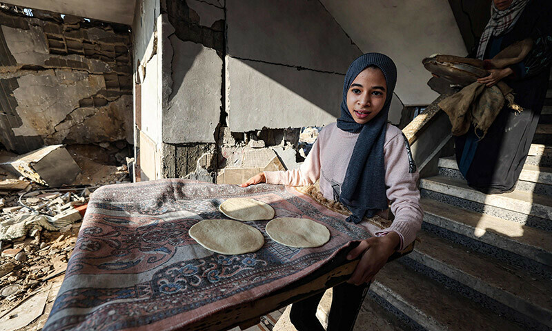 A mother and her daughter prepare traditional unleavened bread in their destroyed house in Rafah in the southern Gaza Strip on December 18, 2023. &mdash; AFP
