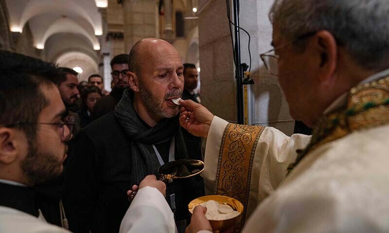 A Latin bishop gives holy bread to a worshiper during the Christmas midnight Mass at the Church of the Nativity compound in the biblical city of Bethlehem in the occupied West Bank on December 25, 2023 &mdash; AFP