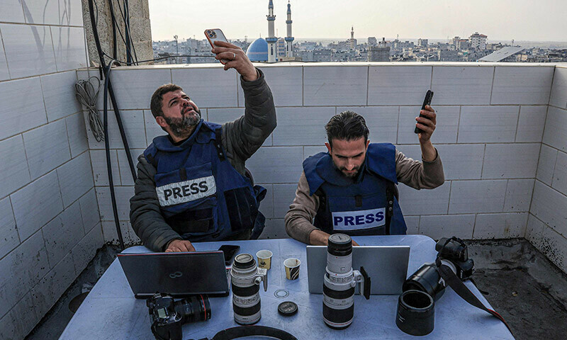 Palestinian journalists attempt to connect to the internet using their phones in Rafah on the southern Gaza Strip on December 27, 2023. &mdash; AFP