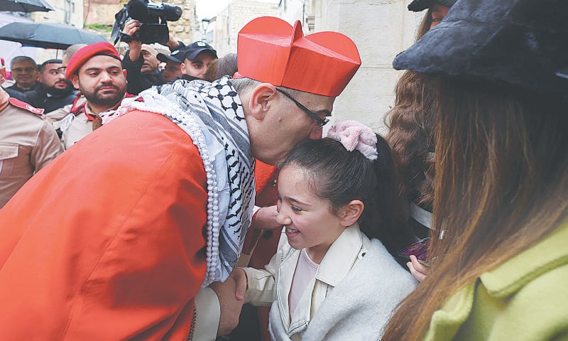 Occupied West Bank: Pierbattista Pizzaballa, the Latin patriarch of Jerusalem, sports a keffiyeh as he blesses a child during his visit to the Old City of Bethlehem to attend Christmas events, on Sunday.&mdash;Reuters