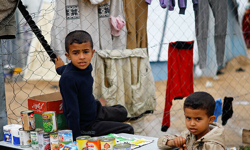 A child sits on a table with tins of food, as displaced Palestinians, who fled their homes due to Israeli strikes, shelter at a tent camp in Rafah, southern Gaza Strip, January 2, 2024. &mdash; Reuters