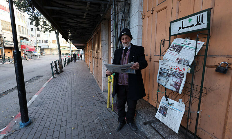 A Palestinian man reads a newspaper near closed shops, during a strike as a protest against the killing of senior Hamas official, Saleh al-Arouri, in Hebron in the Israeli-occupied West Bank January 3, 2024. &mdash; Reuters