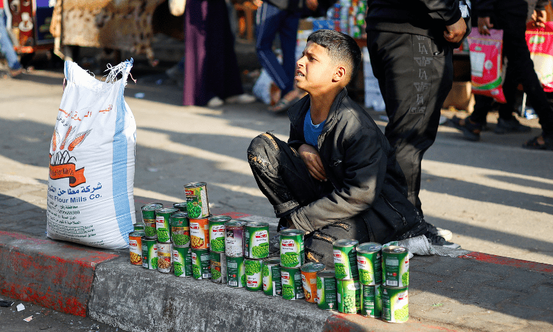  A Palestinian child kneels behind tins of food at a market in Rafah, in the southern Gaza Strip on Jan 4, 2024.  &mdash; Reuters 