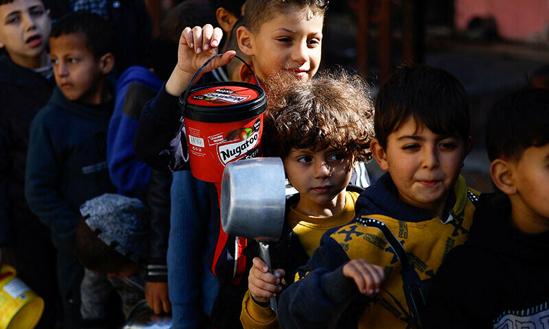 Palestinians wait to receive food cooked by a charity kitchen amid shortages of food supplies in Rafah in the southern Gaza Strip on January 16. &mdash; Reuters