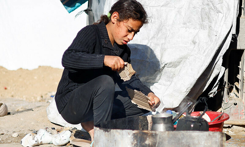 A girl tears a piece of cardboard next to a temporary cooking set up as displaced Palestinians, who fled their houses due to Israeli strikes, shelter at a tent camp in Rafah in the southern Gaza Strip on January 18. &mdash; Reuters