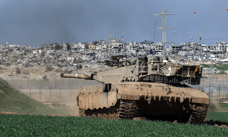 A picture taken from a position in southern Israel along the border with the Gaza Strip on Jan 18, 2024, shows an Israeli tank rolling along the fence and damaged buildings in Gaza. &mdash; AFP 