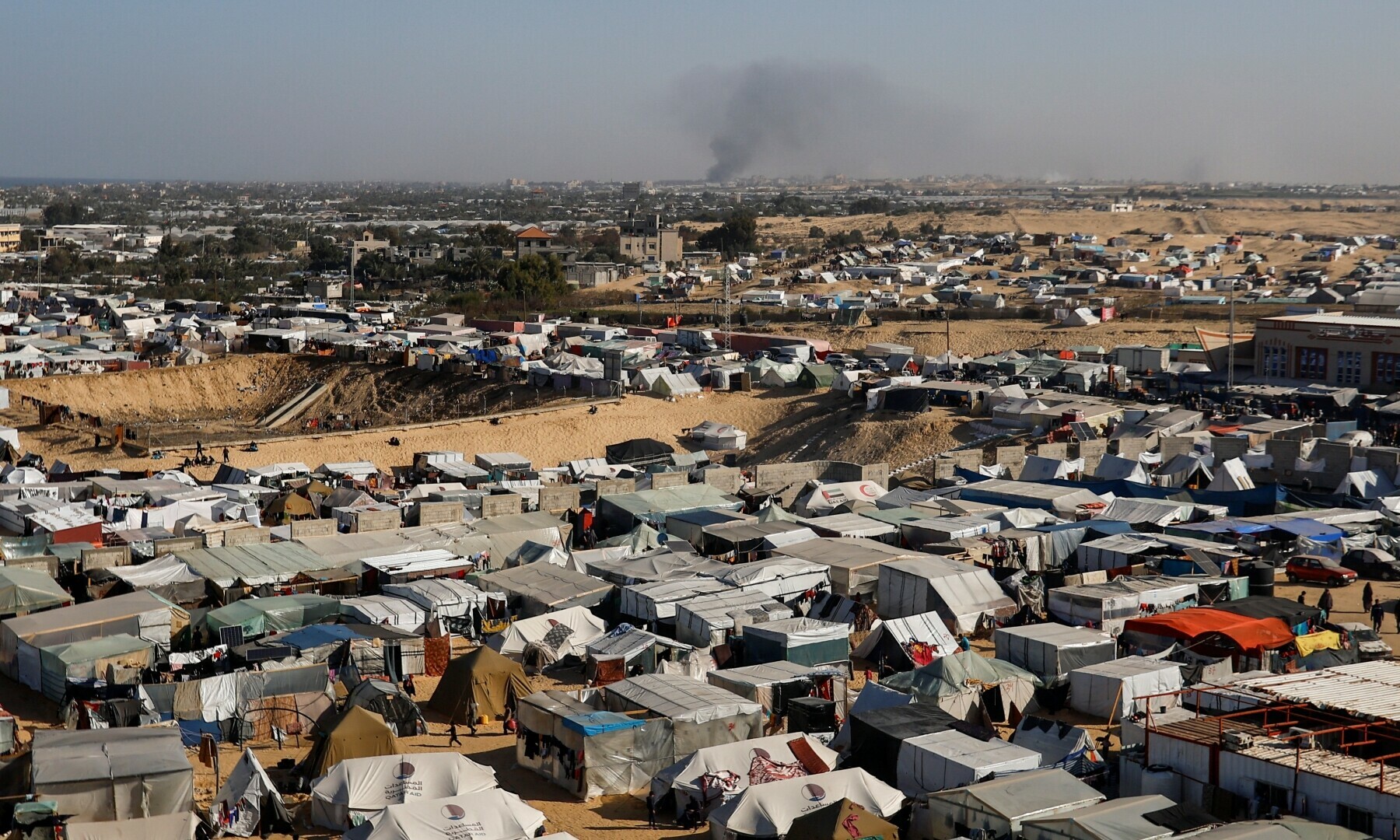 A general view of a tent camp housing displaced Palestinians, as smoke rises in the distance due to an Israeli ground operation in Khan Younis. — AFP
