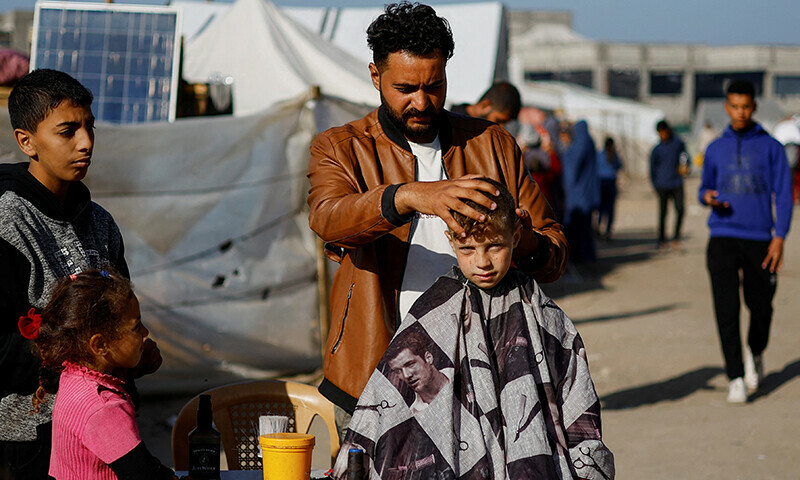 A Palestinian man gives a haircut to a child inside a tent camp housing displaced Palestinians, who fled their houses due to Israeli strikes, amid the ongoing Israeli bombardment in Rafah in the southern Gaza Strip on January 22.&mdash; Reuters