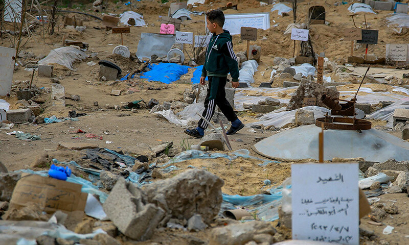 A Palestinian boy walks inside a makeshift cemetary where people killed in Israeli bombing are buried in shallow tombs, in Gaza City&rsquo;s Al-Sahaba Street, on January 9. &mdash; AFP