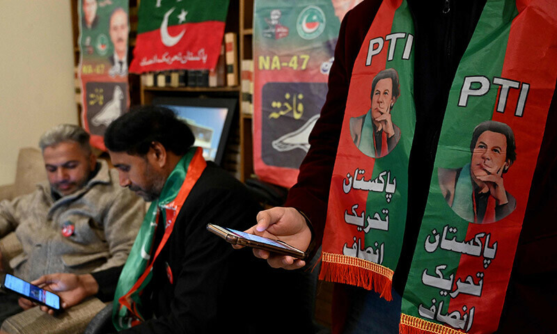 Former prime minister Imran Khan&rsquo;s supporters wear scarves with prints of PTI as they listen to a virtual election campaign on phones at the party&rsquo;s office in Islamabad on February 3. &mdash; AFP