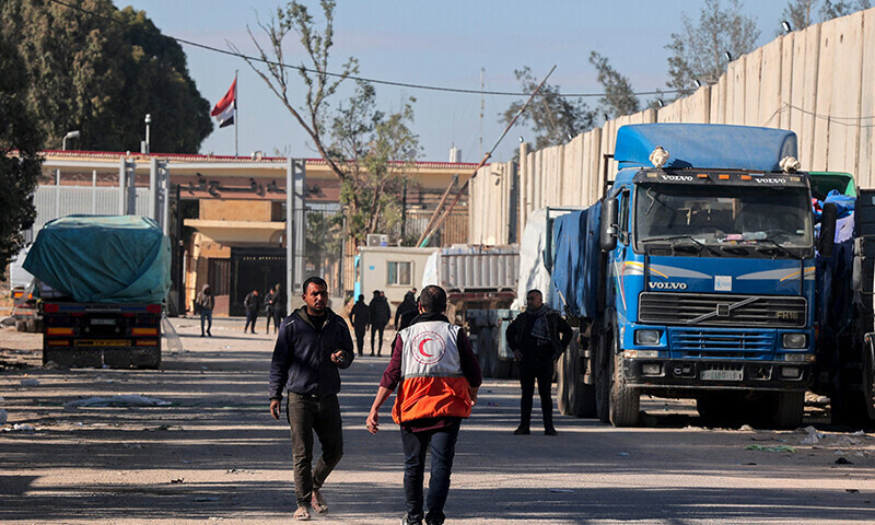 People walk past trucks carrying humanitarian aid that entered Gaza by truck through the Kerem Shalom (Karm Abu Salem) border crossing in the southern part of the Palestinian territory on February 17, 2024, as they wait to be unloaded on the Palestinian side of the Rafah border crossing with Egypt (background), amid the ongoing conflict between Israel and Hamas. &mdash; AFP