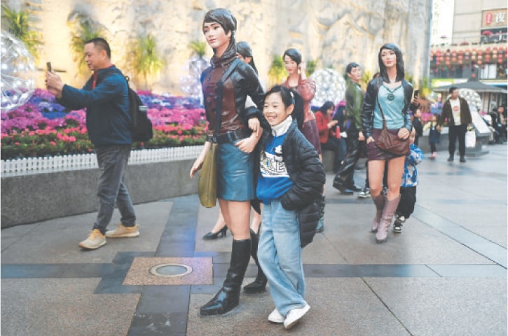 Chengdu (Sichuan province): A child poses for a picture with a statue along a business street on the ninth day of the Lunar New Year of the Dragon, on Sunday.&mdash;AFP