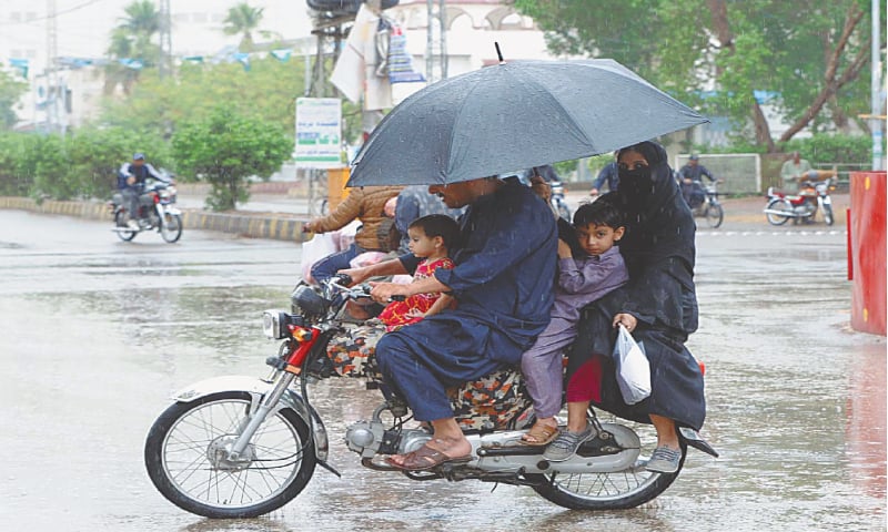 HYDERABAD: A woman holds an umbrella while riding a motorbike with her family in a bid to keep them dry during rain on Friday.&mdash;Online