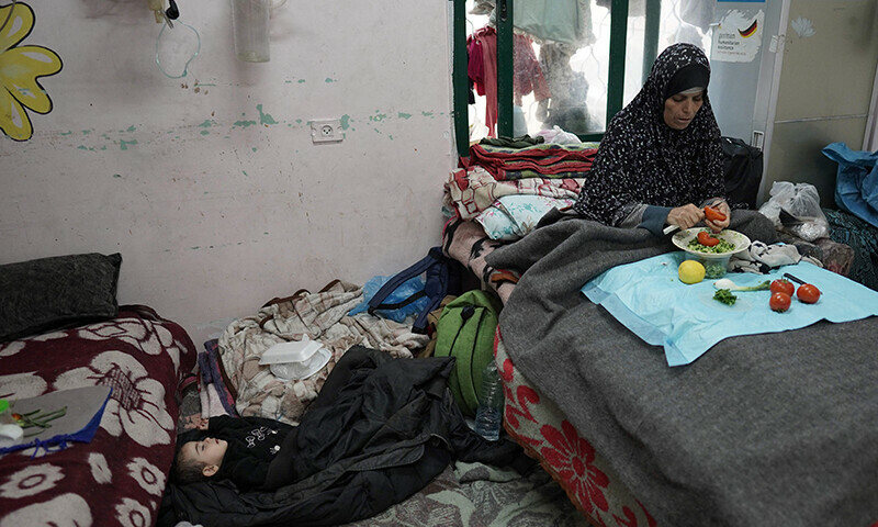 A Palestinian woman cuts vegetables near a sleeping boy at the Shuhada Al Aqsa Hospital in Deir el-Balah in the central Gaza Strip on April 3. &mdash; AFP