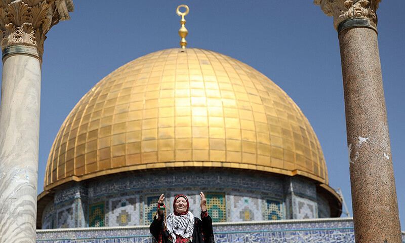 A Palestinian woman dressed in a traditional embroidered dress raises her arms in prayer as she stands in front of the Dome of the Rock mosque in Jerusalem during the last Friday prayer of Ramazan on April 5, 2024.&mdash;AFP