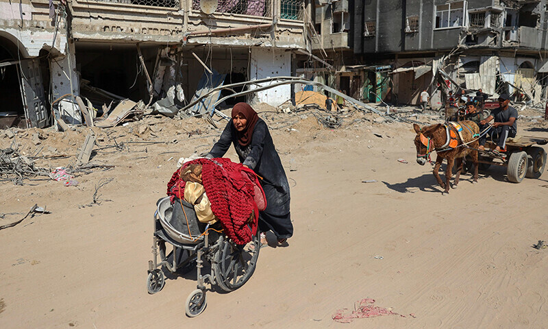 A Palestinian elderly woman uses a wheelchair to ferry her belongings past damaged buildings in Khan Younis on April 7 after Israel pulled troops out of the southern Gaza Strip. &mdash; AFP