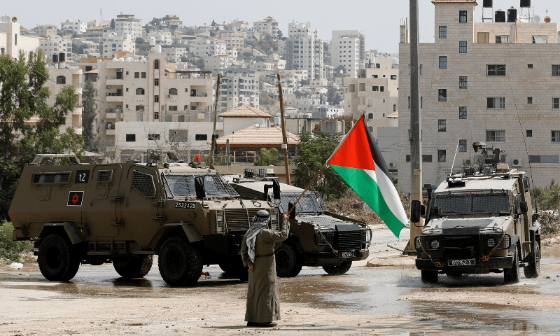  A man holds the Palestinian flag next to Israeli military vehicles during a raid in Tulkarm, in Israel-occupied West Bank on Aug 22, 2024. &mdash; Reuters 
