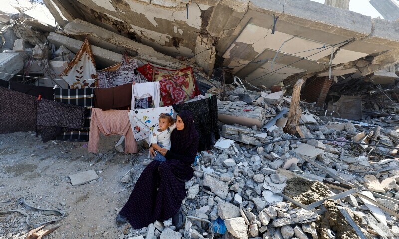 A Palestinian woman sits with a child next to rubble of a house destroyed in Israel&rsquo;s military offensive, amid the ongoing conflict between Israel and Hamas, in Khan Younis in the southern Gaza Strip October 7, 2024. &mdash; Reuters